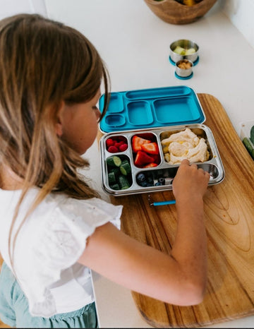 Introducing the Lunch Buddy Bento Set by The Play Way, a sleek rectangular stainless steel lunchbox with multiple compartments. The top right section is larger than the others, with "TPW" engraved in the central compartment. It features a silicone seal lid, rounded edge design, clasp closure, and a polished metallic finish.