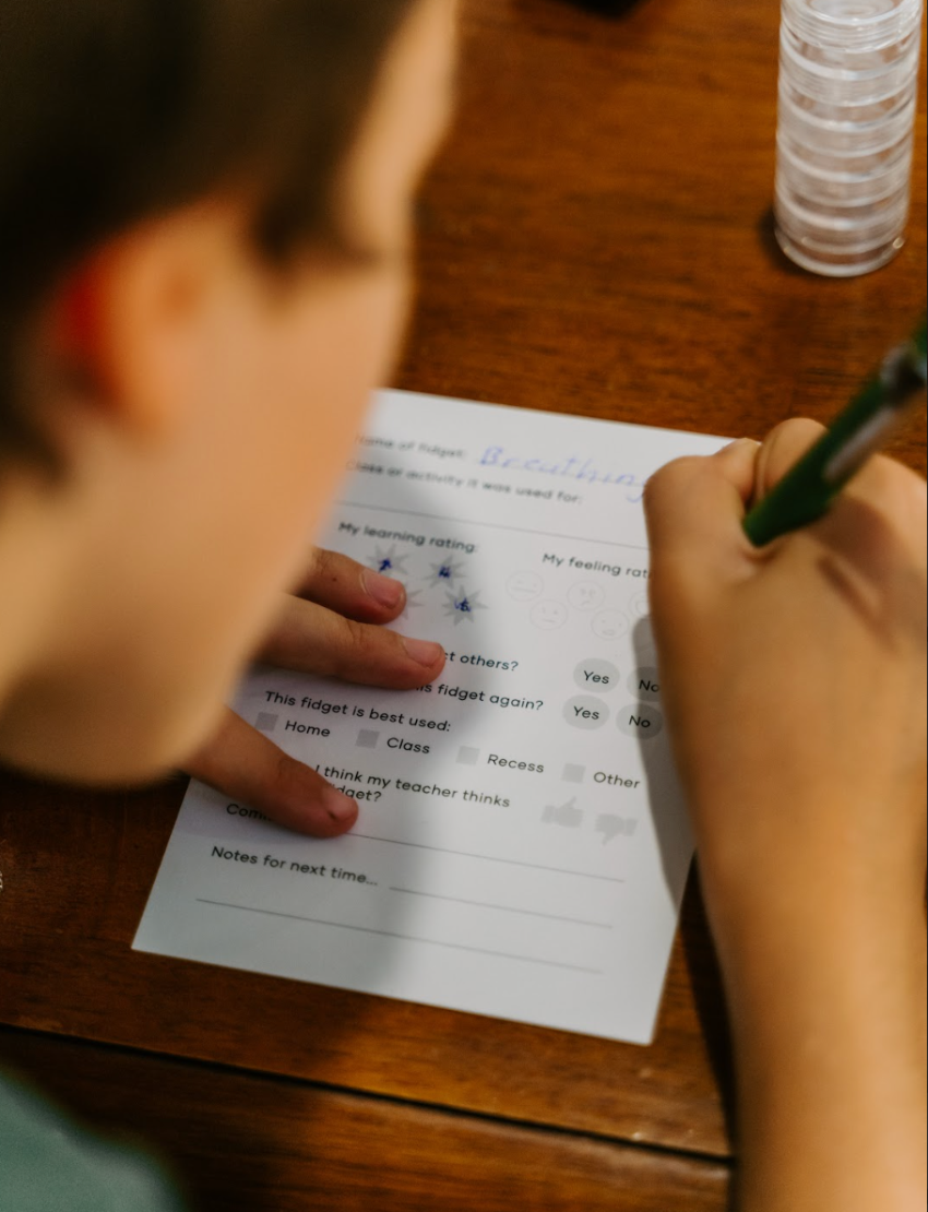 The Regulation and Reflection Kit by The Play Way contains various educational and sensory items. Visible items include a book titled "STIMS, SCHOOL & ME," breathing cards, a mini MP3 player, reflective journal cards, a sensory play kit, and a book titled "The Buzzing Busy Brain.