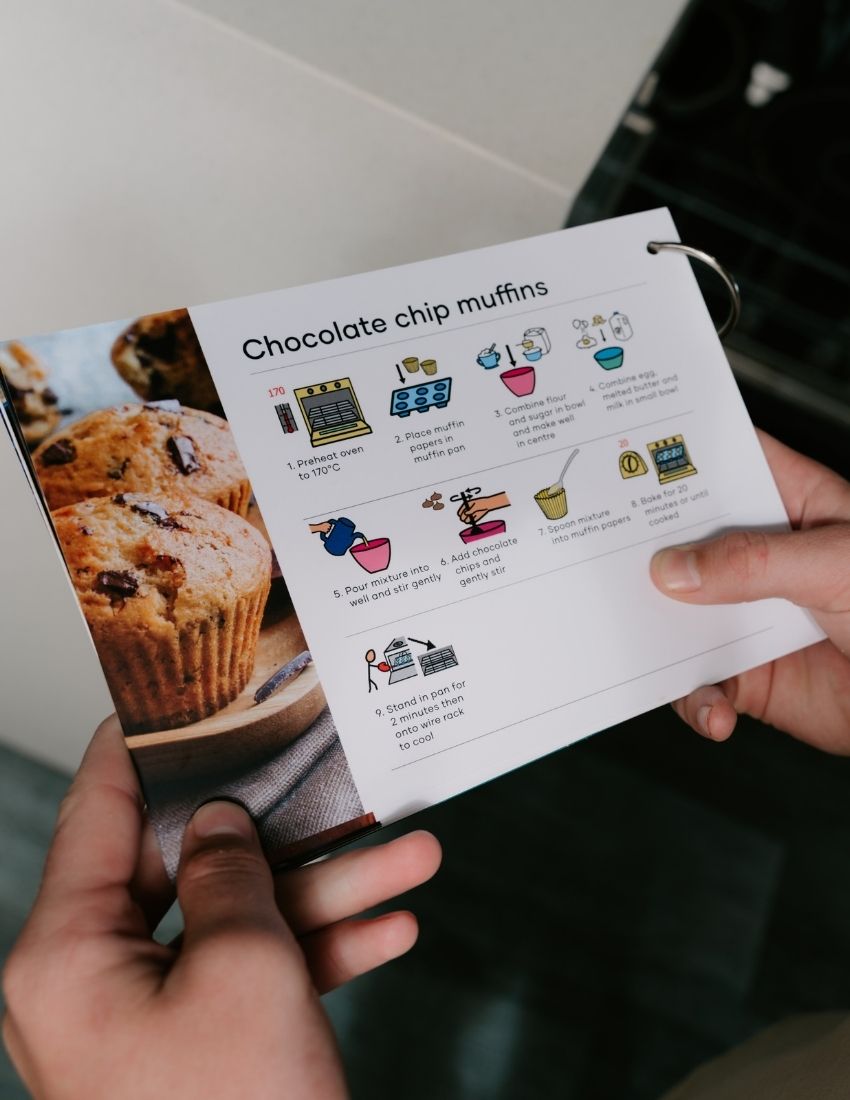 A set of "Cooking for Independence Recipe Cards" by The Play Way is displayed on a light background. The top card showcases the product title with vibrant abstract shapes. Behind it, three cards are partially visible, featuring a chocolate chip muffin recipe and dishwashing instructions to enhance cooking skills.