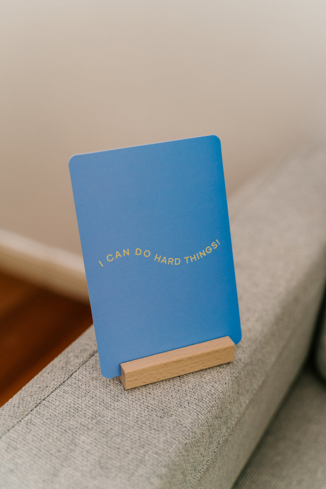 Two teal items are pictured: a rectangular box labeled "Affirmation Card Set with Timber Card Holder" and a smaller booklet with the same label. The booklet, titled "Sensory Play," by The Play Way, promotes emotional balance. Both items rest against a plain white background, inviting a growth mindset.