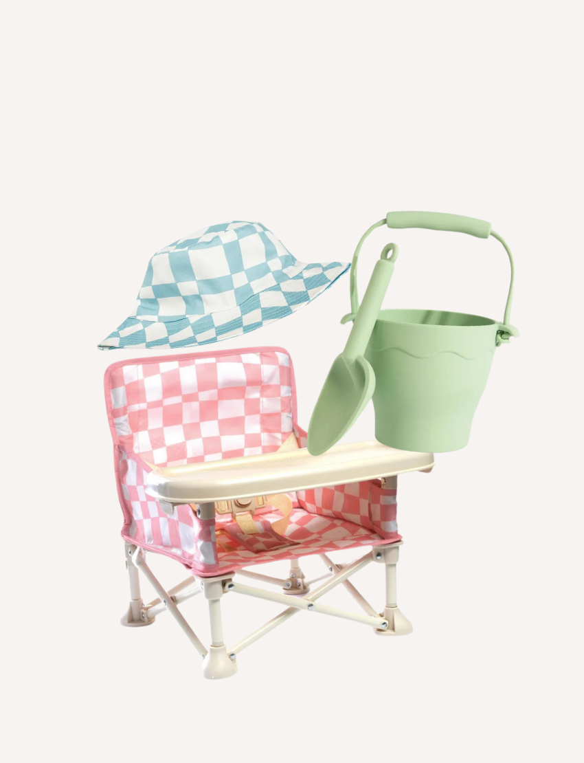 The "Beach with Little Ones Bundle" by The Play Way includes the Izimini Baby Chair with a pink and white checkered pattern and built-in tray, a green Bucket & Spade Set, and a cozy blue and white checkered baby cotton hat, all set against a plain background.
