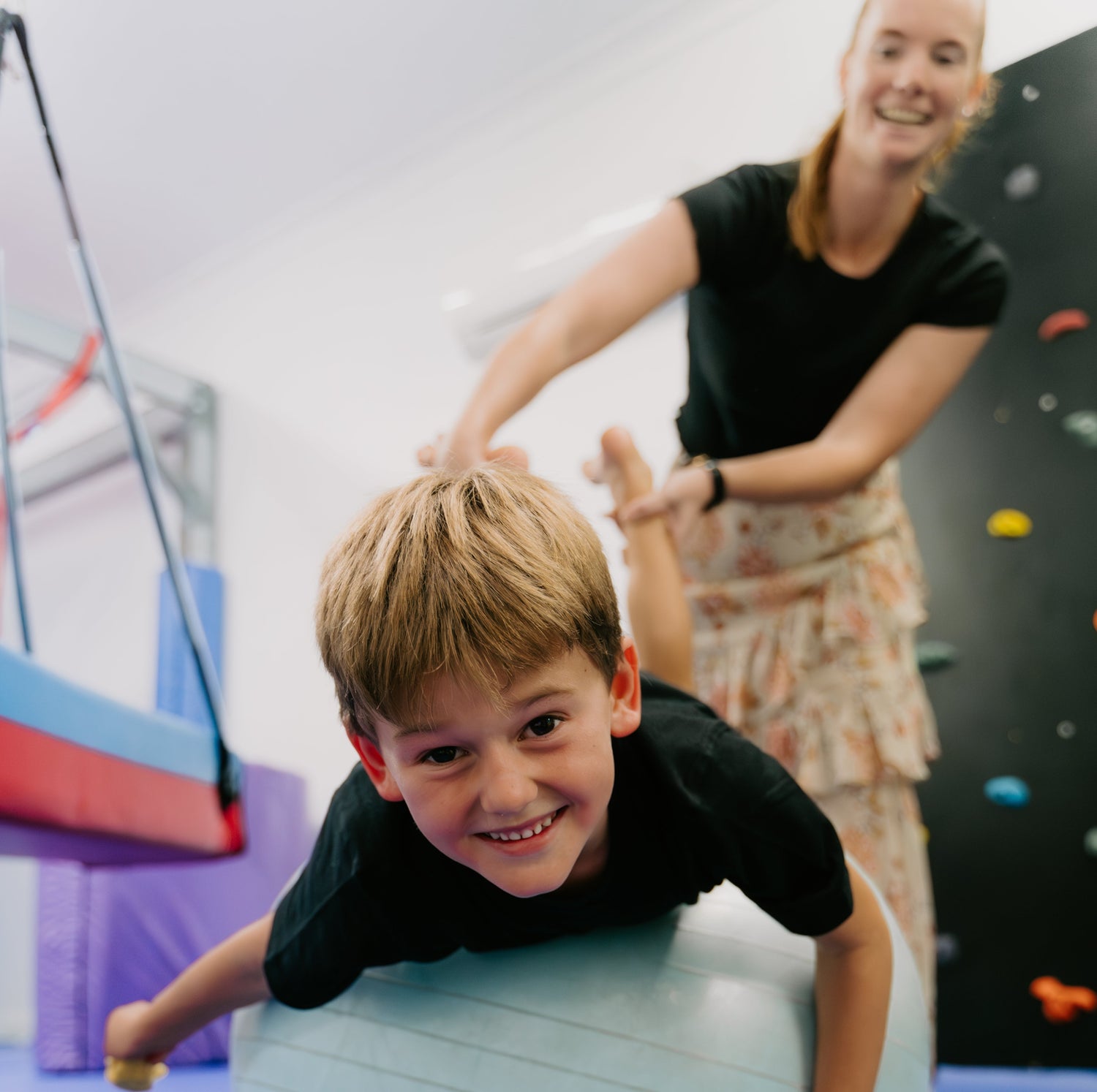 Child playing on a large exercise ball with an adult in a gym setting