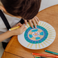 The Creative Mindfulness: Mandalas Program by The Play Way includes a vibrant open box with markers, colored pencils, notebooks, paint, a tote bag, and crafting materials. It has abstract green, purple, and orange patterns with "The Play Way" text.