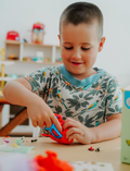The Therapy At Home Fine Motor Advanced Program features a vibrant box with modeling clay, a 3D paper model kit, cards, stickers, markers, and more—ideal for building fine motor skills as recommended by occupational therapists.
