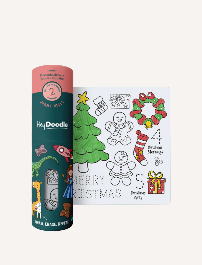 The HeyDoodle Mini Mat - ABC - Jingle Bells is on display, featuring a rolled tube labeled "HeyDoodle" alongside a flat mat. The mat is decorated with illustrations of a Christmas tree, gingerbread figures, stockings, wreaths, and gifts, providing spaces for coloring and drawing.