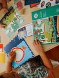 Children are seated at a table, engrossed in the Mosaic Sticker Art - Animal Homeland by Jar Melo. In front of them are vibrant boards and sheets filled with stickers showcasing animals such as crocodiles and fish. Their hands are busy applying the stickers to complete the designs.