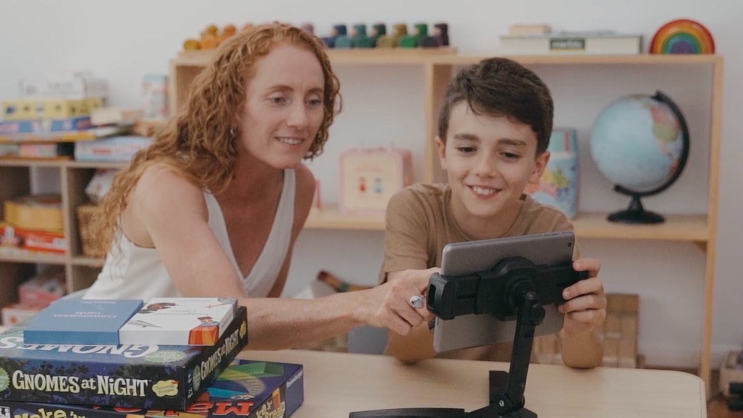 Two people sitting at a table with board games and a tablet.