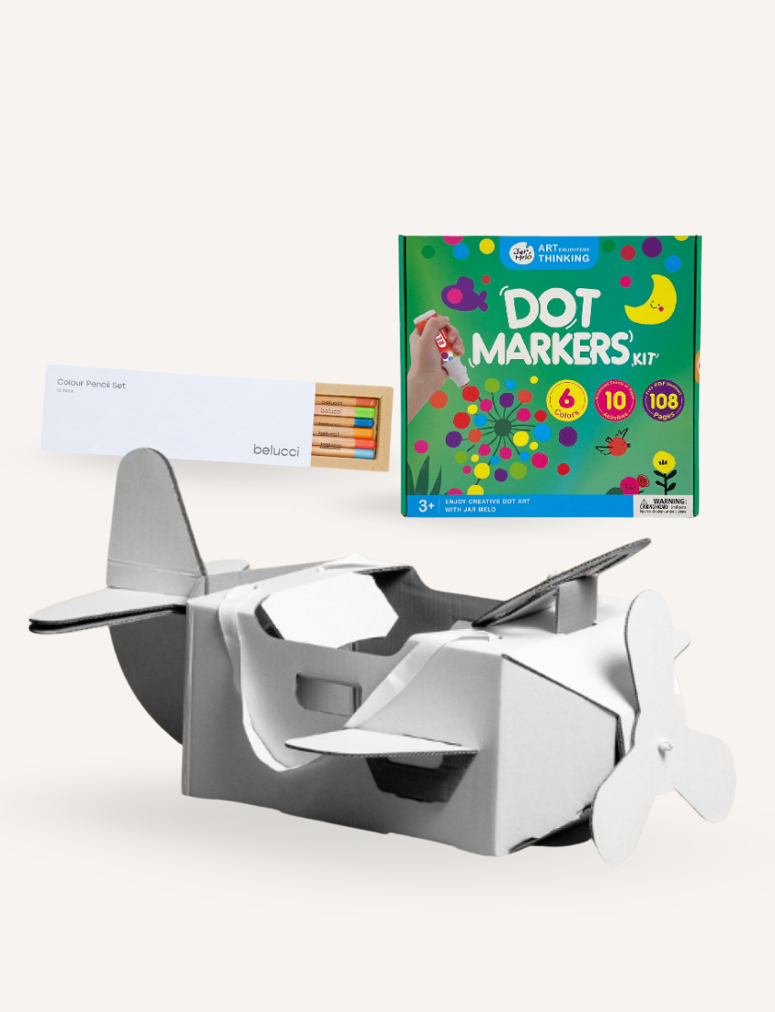 A white box of "beloci" colored pencils is on the left, a vibrant Dot Markers Kit from The Play Way's Little Artist Creative Bundle is on the right, and a cardboard airplane model for creative costumes awaits in front.