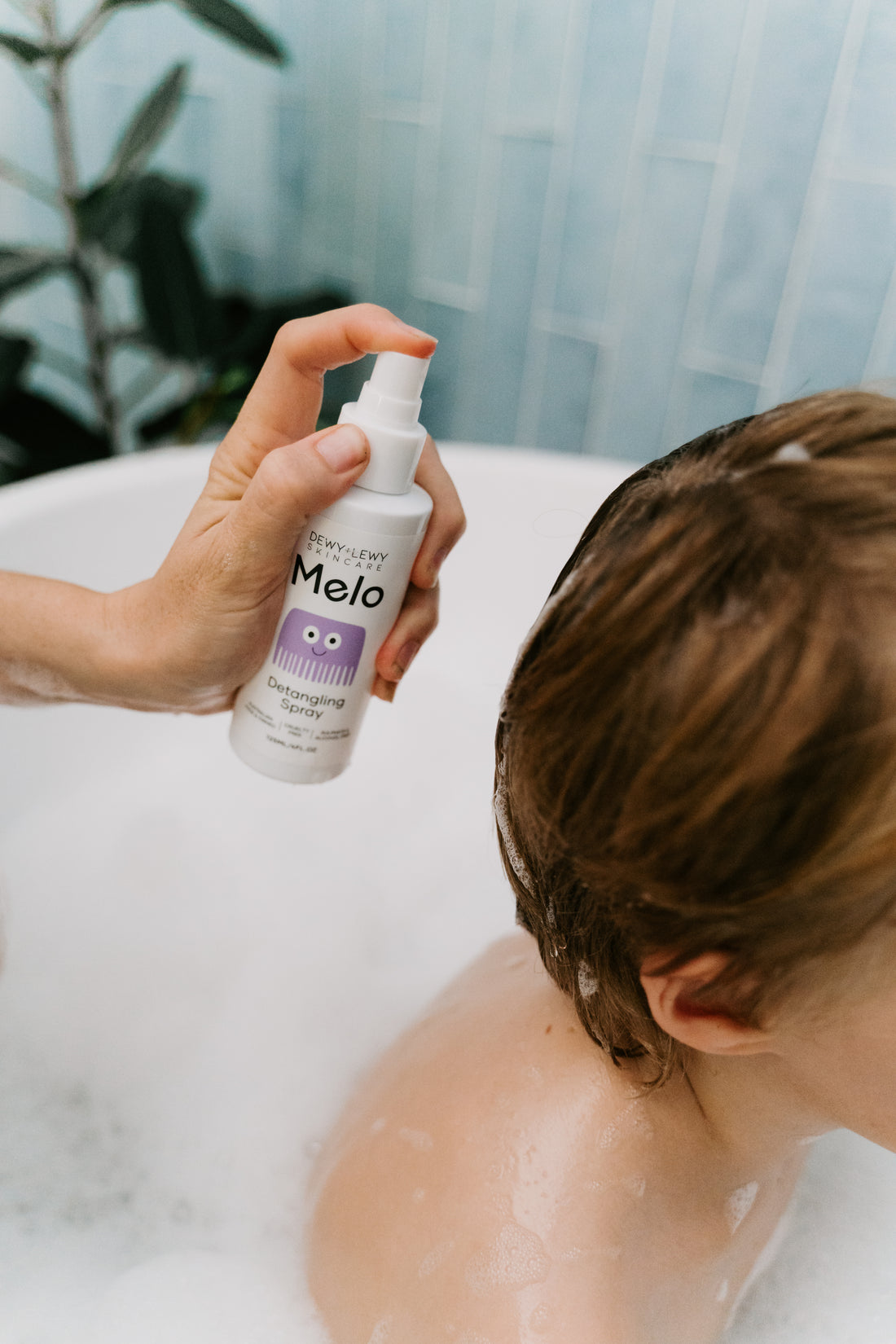 Two white spray bottles with purple labels of Melo Detangling Spray by Melo, each containing 135ml (4.6oz). The front bottle displays the product name along with an illustration of a purple comb, while the back bottle provides usage instructions, ingredients, and emphasizes its cruelty-free organic formula designed for children's hair care.