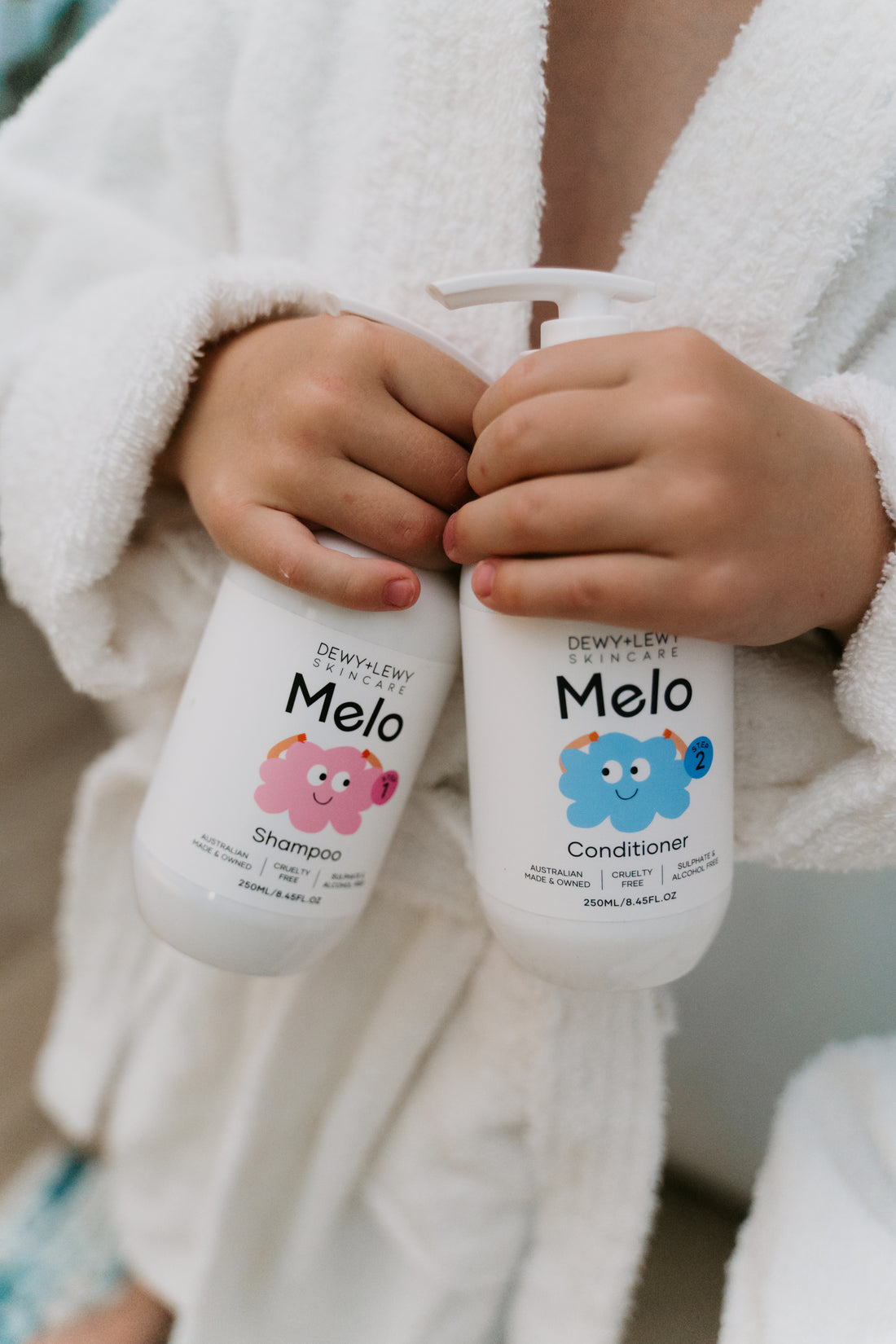 Two bottles of Melo's Melo Conditioner are displayed. One bottle faces forward, showcasing the product label, while the other faces backward, displaying the ingredient list and information. Both bottles, designed for babies with a gentle formula, feature white pumps and are paraben-free.