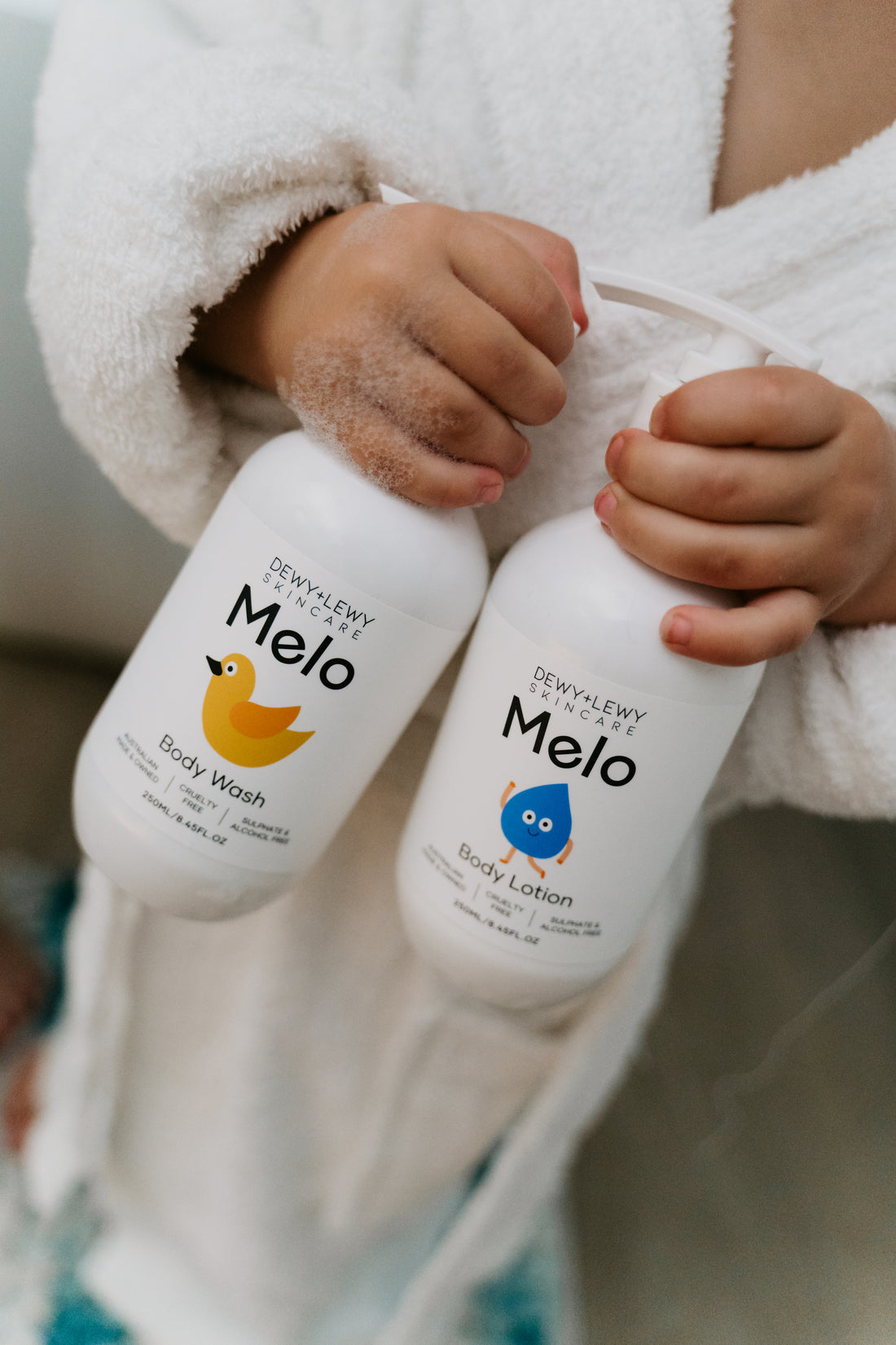 Two white pump bottles of Melo's Melo Body Lotion are shown. The front bottle displays the product name and a blue droplet logo, while the back bottle lists the ingredients and usage instructions. Both 250ml/8.45fl oz bottles are ideal for sensitive skin and proudly cruelty-free.