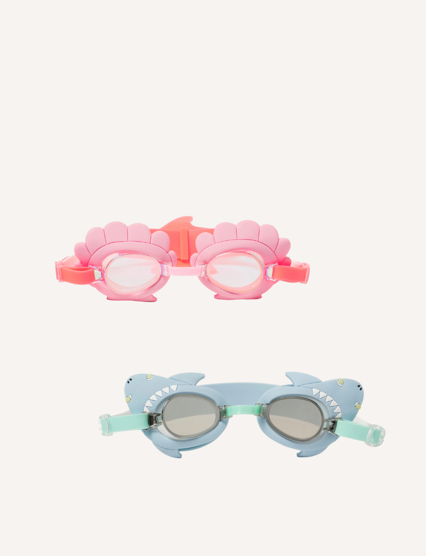 On a plain background, two pairs of Sunnylife's Mini Swim Goggles are displayed. The top pair is pink adorned with a shell design, while the bottom pair is blue with intricate shark details, including fins and teeth.