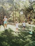 Two kids are smiling and posing outdoors with their arms around each other while holding paddles and balls from the Ollie & Jack LED Pickleball Net Set. They are dressed in casual summer clothing and caps, with greenery in the background beneath a sunny sky.