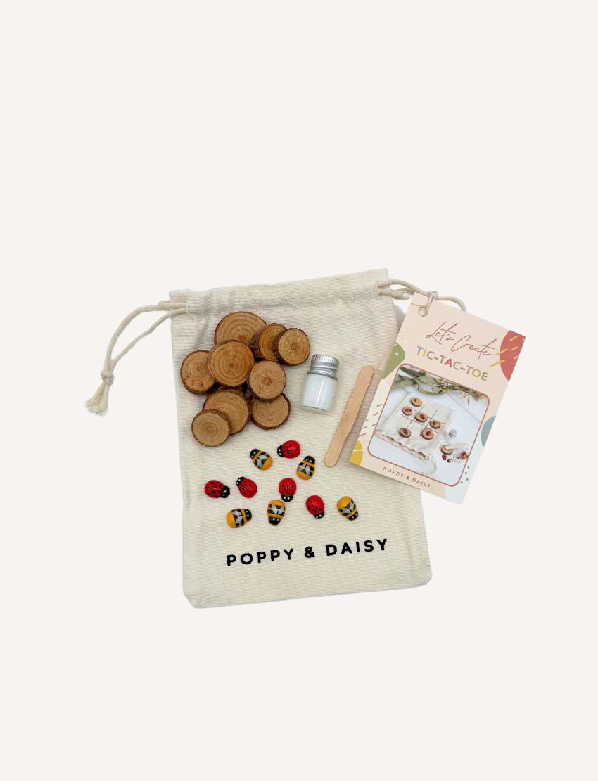 Poppy & Daisy DIY Tic-Tac-Toe kit with drawstring bag, wooden slices, charms, paint, and instructions.