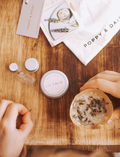 A hand holds a small tin of Lavender Lip Balm. Below it, a cloth pouch labeled 