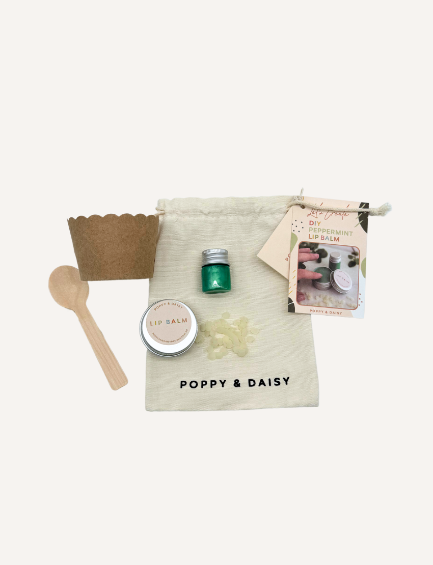 The Peppermint Lip Balm kit by Poppy & Daisy contains a cloth bag with the brand's label, a small jar of lip balm, a metal jar featuring a label, a wooden spoon, a scalloped paper cup, a small green bottle, and an instruction card complete with a photo.