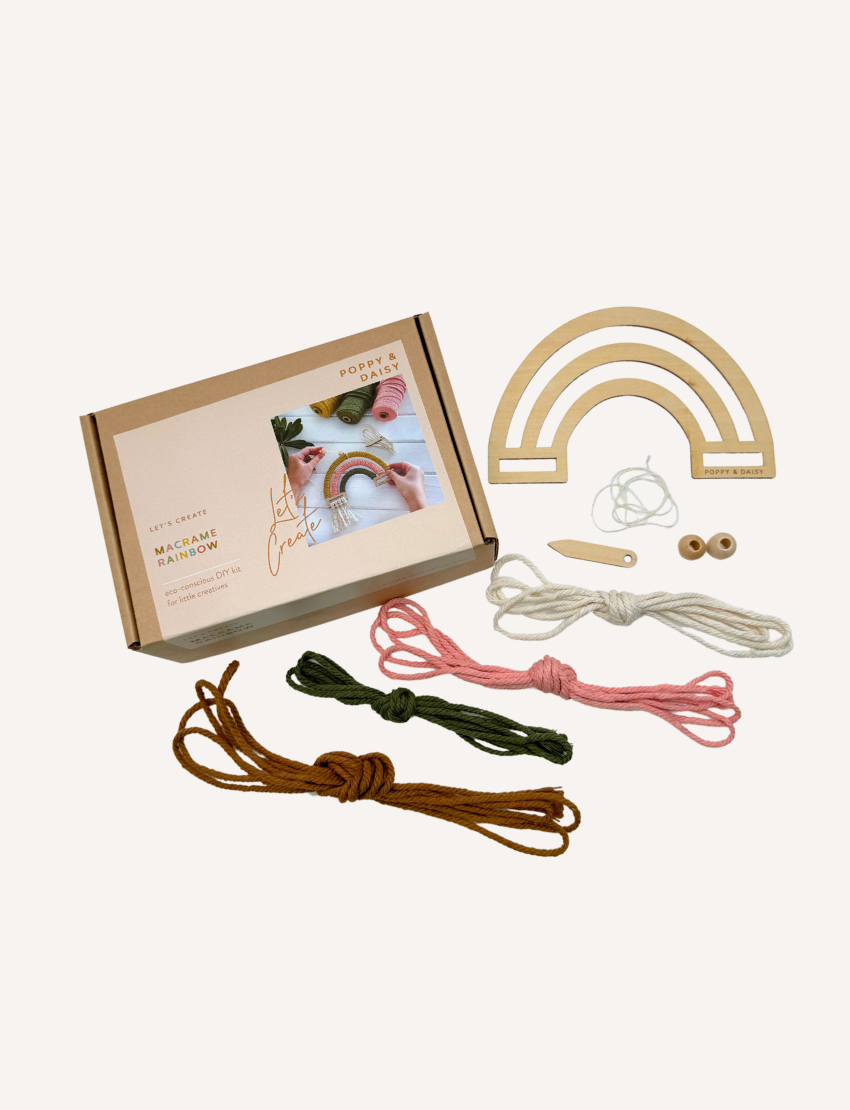 Poppy & Daisy Macrame Rainbow DIY Kit: includes cardboard box, wooden rainbow shape, yarn, beads, and instructions.