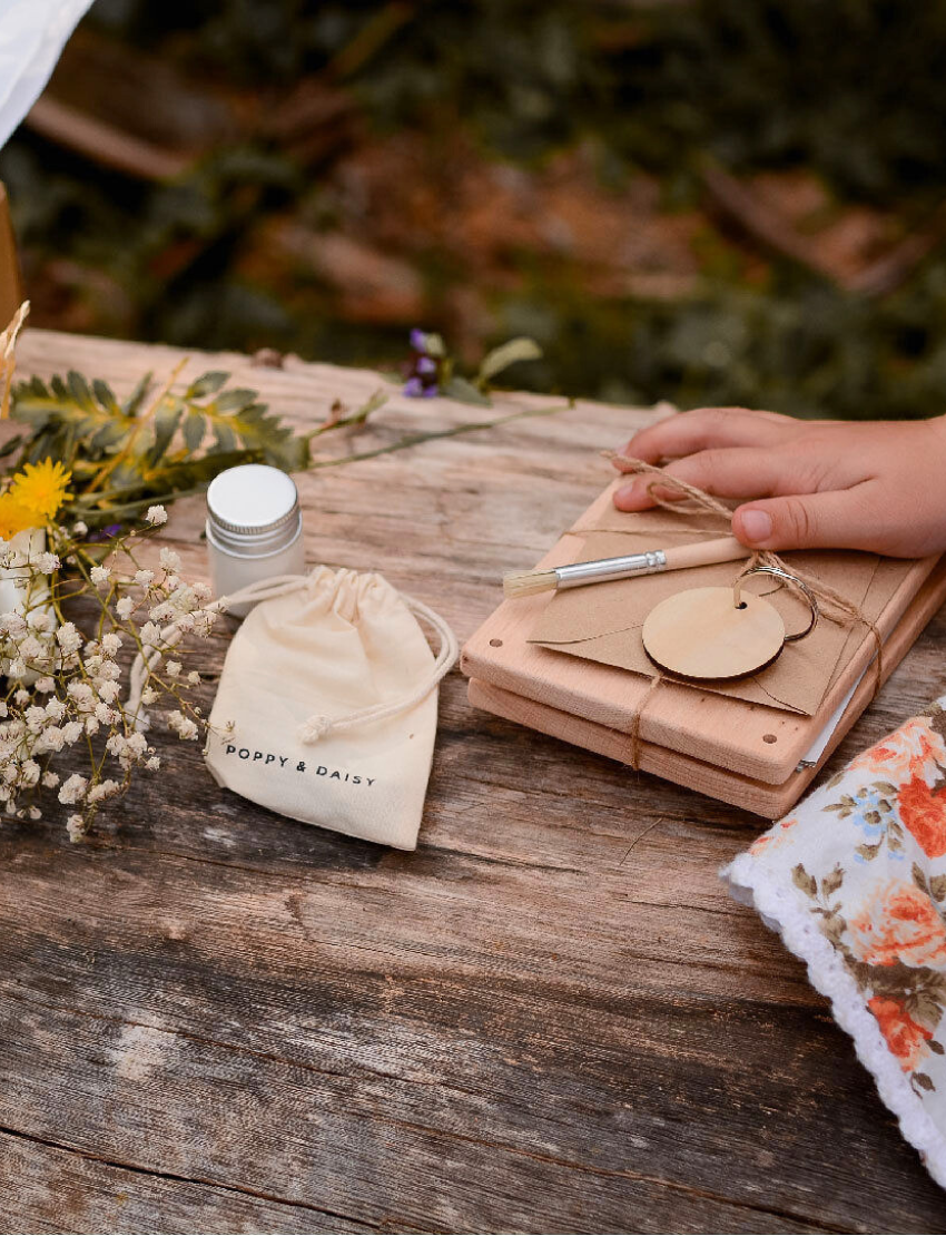 The Poppy & Daisy Flower Press kit is perfect for creating pressed flowers and includes wooden boards engraved with "Poppy & Daisy" text, a small jar, screws, a pencil, a blank round keychain as a unique keepsake, and a craft envelope. The packaging features an illustrated label with a floral pressing design.