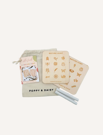 A person is holding a collection of nature-themed cards from Poppy & Daisy's "Nature Hunt" set, which includes sketches of insects and plants. Accompanying the cards are two pieces of white chalk and a fabric pouch, all set against a grassy background.