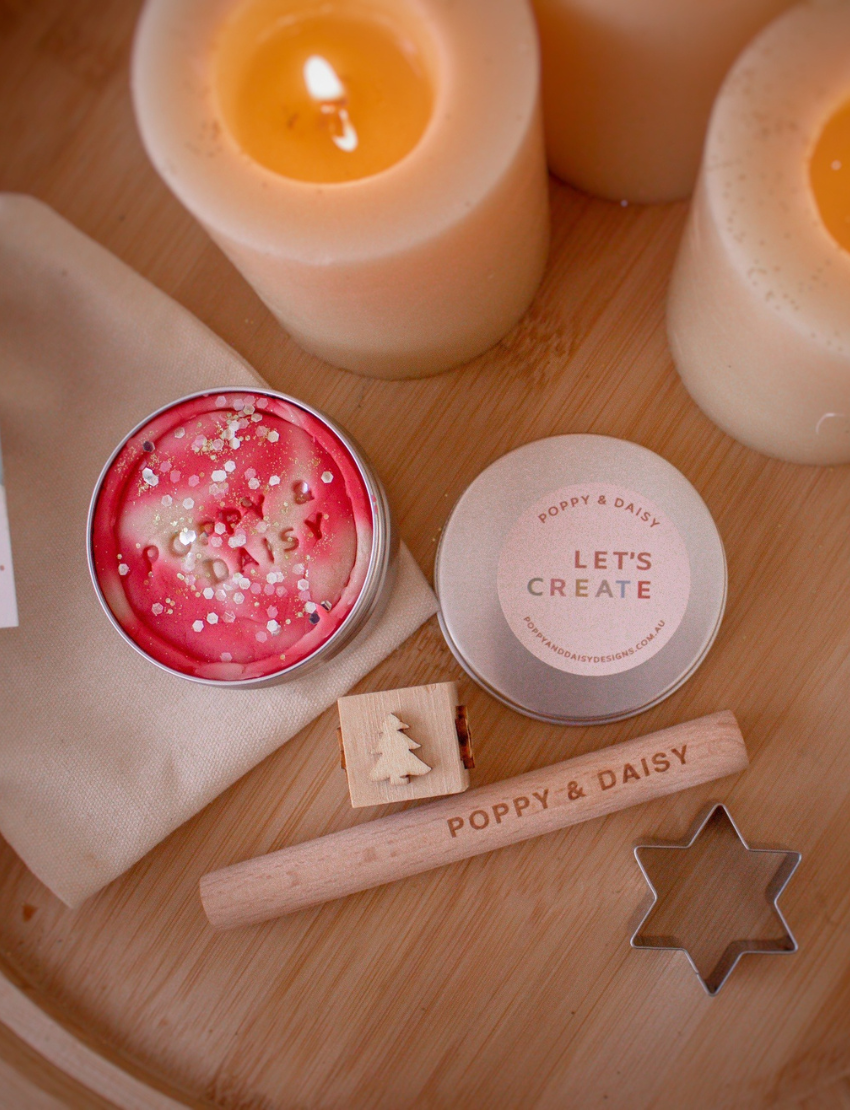 A child uses a star-shaped cutter to cut out star shapes from Poppy & Daisy's Candy Cane Playdough on a marble board, while pinecones, greenery, a wooden roller, and string lights in the background enhance the festive atmosphere.