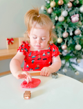 A child uses a star-shaped cutter to cut out star shapes from Poppy & Daisy's Candy Cane Playdough on a marble board, while pinecones, greenery, a wooden roller, and string lights in the background enhance the festive atmosphere.