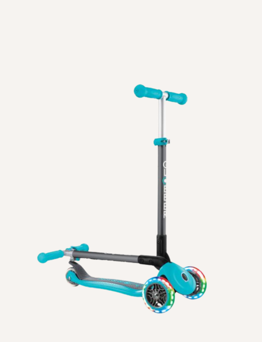 The PRIMO Foldable Lights Scooter by Globber is a blue children's scooter featuring three wheels, a T-shaped handlebar, and LED lights on the front wheels. It boasts a sleek design with a sturdy frame, casting a shadow on the ground.