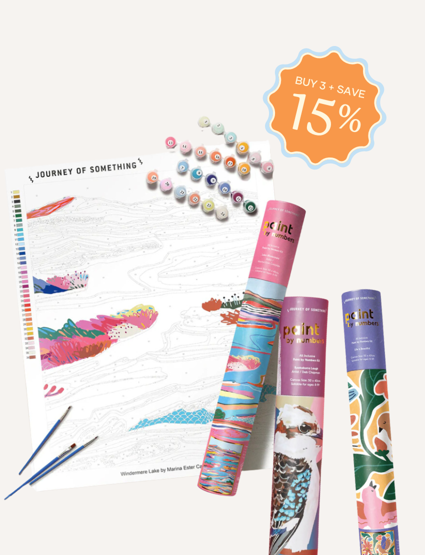 The Journey of Something Paint by Numbers kit includes a rolled canvas featuring butterfly outlines, housed in a blue cylindrical container. The kit also contains numbered paint pots, three paintbrushes, and a reference sheet. The canvas showcases butterflies partially colored in pink and blue hues.