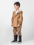 The Cry Wolf Play Jacket in tan is a waterproof hooded raincoat made from eco-friendly, recycled materials. It features a buttoned and zippered front, two flap-front pockets, elastic-cuffed long sleeves for comfort, and a small chest logo.