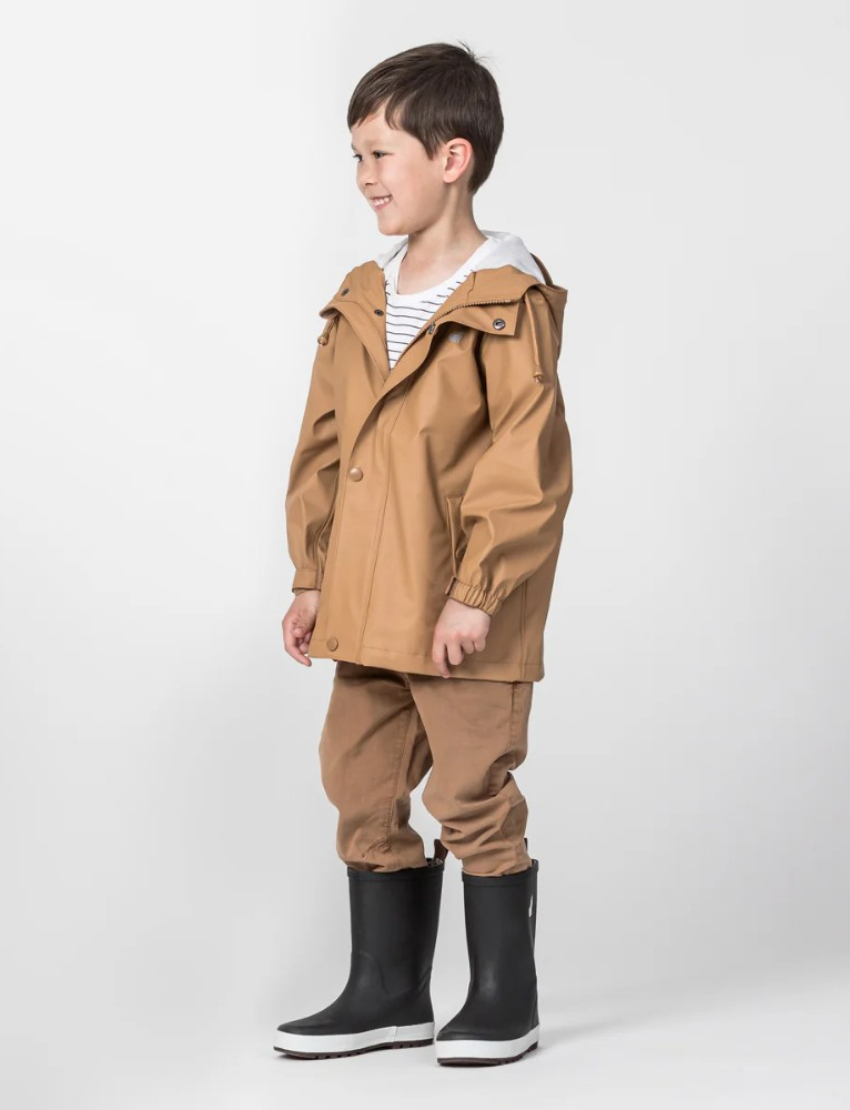 The Cry Wolf Play Jacket in tan is displayed against a white background. The raincoat features a front button closure, drawstrings on the hood, two front pockets with button flaps, and long sleeves with elastic cuffs. A small logo is visible on the left chest area.