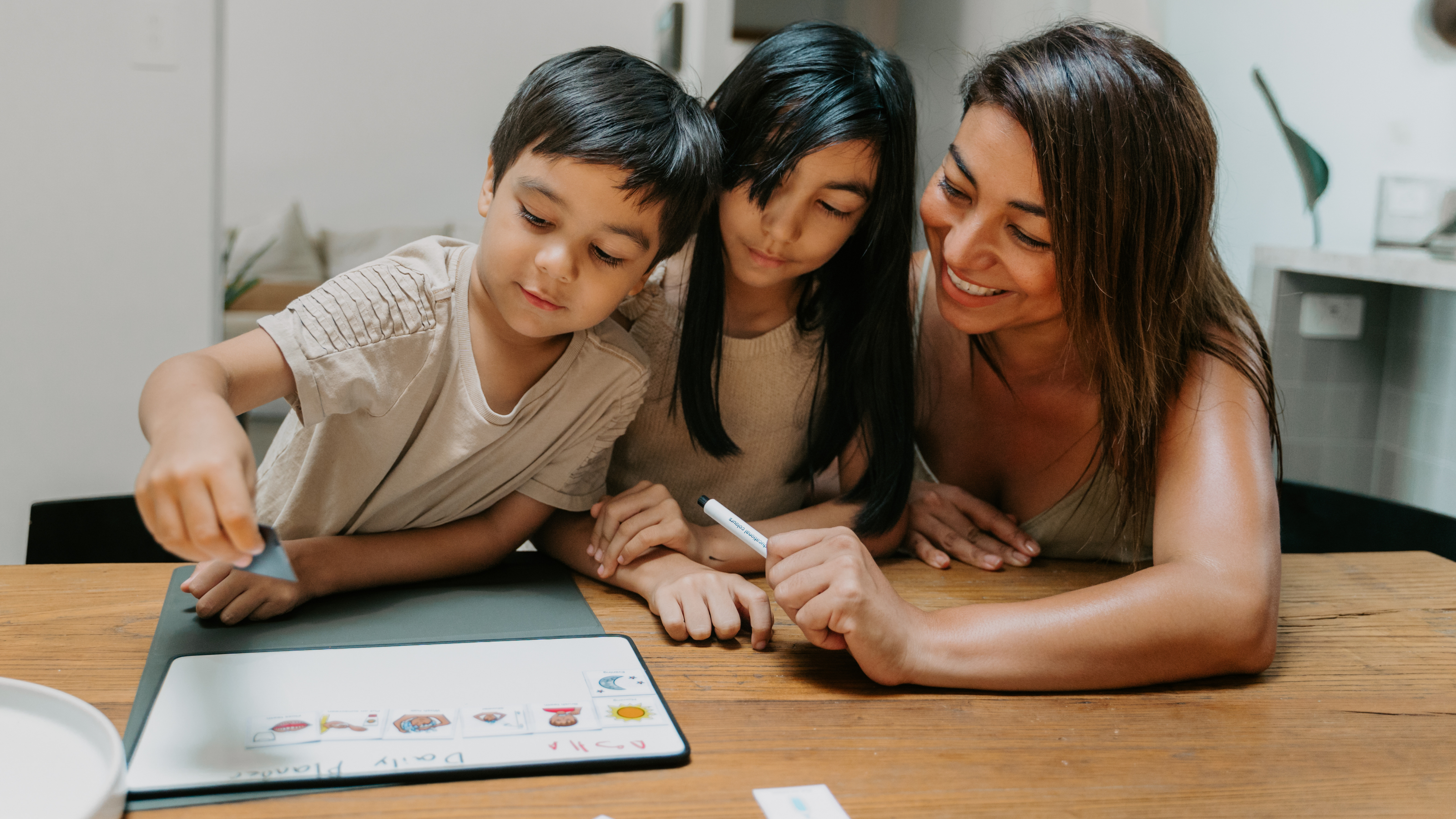 Woman and two children sitting at a table with a tablet, engaged in an activity.