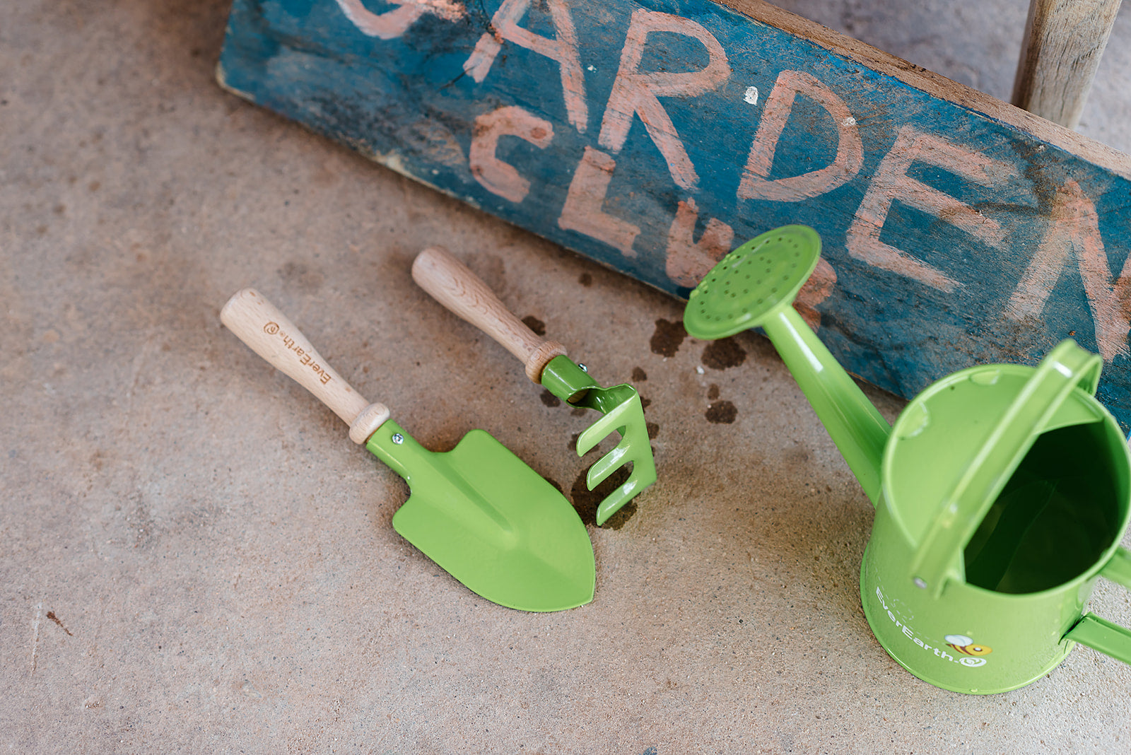The EverEarth Outdoor Gardening Bag With Tools is a green set ideal for children's outdoor play, featuring a watering can, spade, trowel, and small fork with wooden handles. These tools are neatly displayed in front of a canvas tote decorated with green polka dots and multiple pockets.