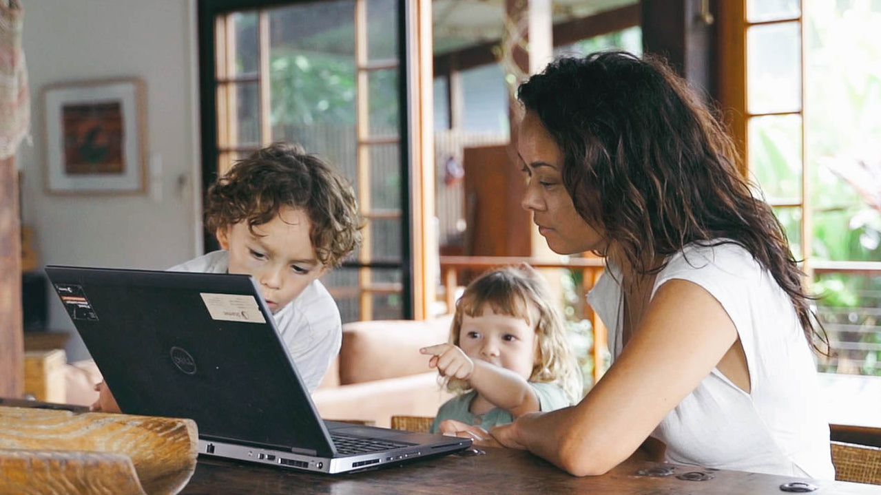 Woman and two children using a laptop together at a wooden table.