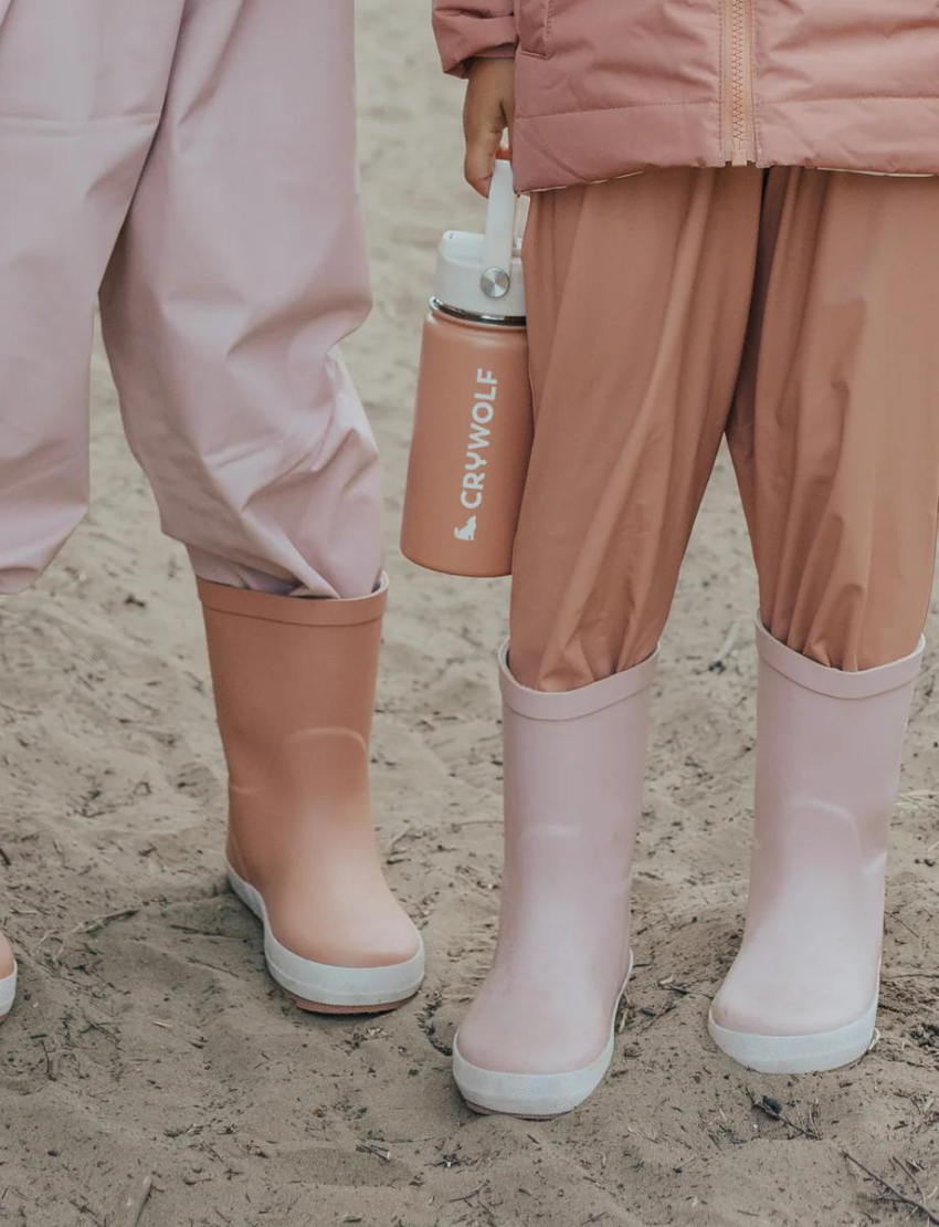 A pair of Cry Wolf's Rain Boots in Dusty Pink, featuring white soles and a small white silhouette of a dog logo on the side. The boots come with pull loops at the top and are showcased against a plain, light background.