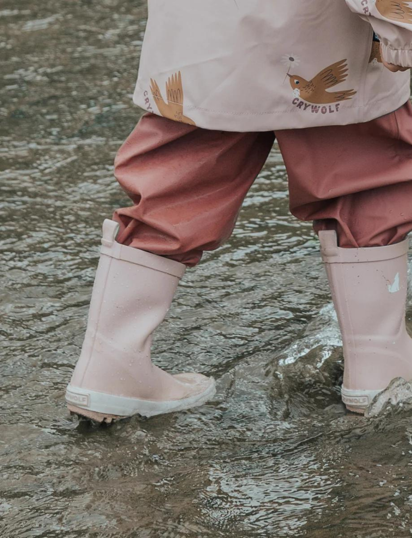 Cry Wolf's Rain Boots - Dusty Pink feature a small white dog silhouette on the side and convenient loop handles. They're crafted from natural rubber, with a white sole and textured grip pattern for secure footing.