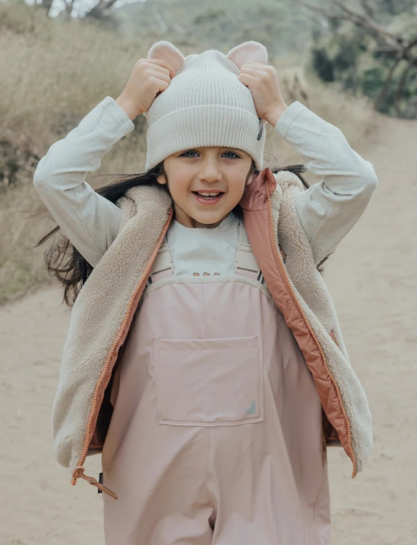 This image shows the back view of the Cry Wolf Rain Overalls in Dusty Pink, designed for children aged 3 years. The overalls feature elasticated cuffs at the ankles and adjustable shoulder straps with the brand's name printed on them. The words "A CRY WOLF" are printed across the back.