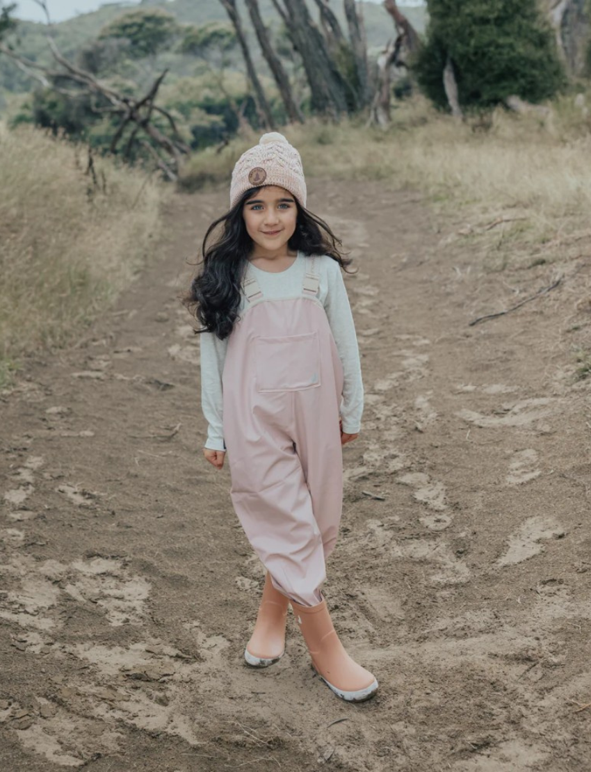 This image shows the back view of the Cry Wolf Rain Overalls in Dusty Pink, designed for children aged 3 years. The overalls feature elasticated cuffs at the ankles and adjustable shoulder straps with the brand's name printed on them. The words "A CRY WOLF" are printed across the back.