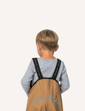 A pair of children's tan waterproof Rain Overalls from Cry Wolf with elasticated ankle cuffs, black adjustable shoulder straps, and the words 