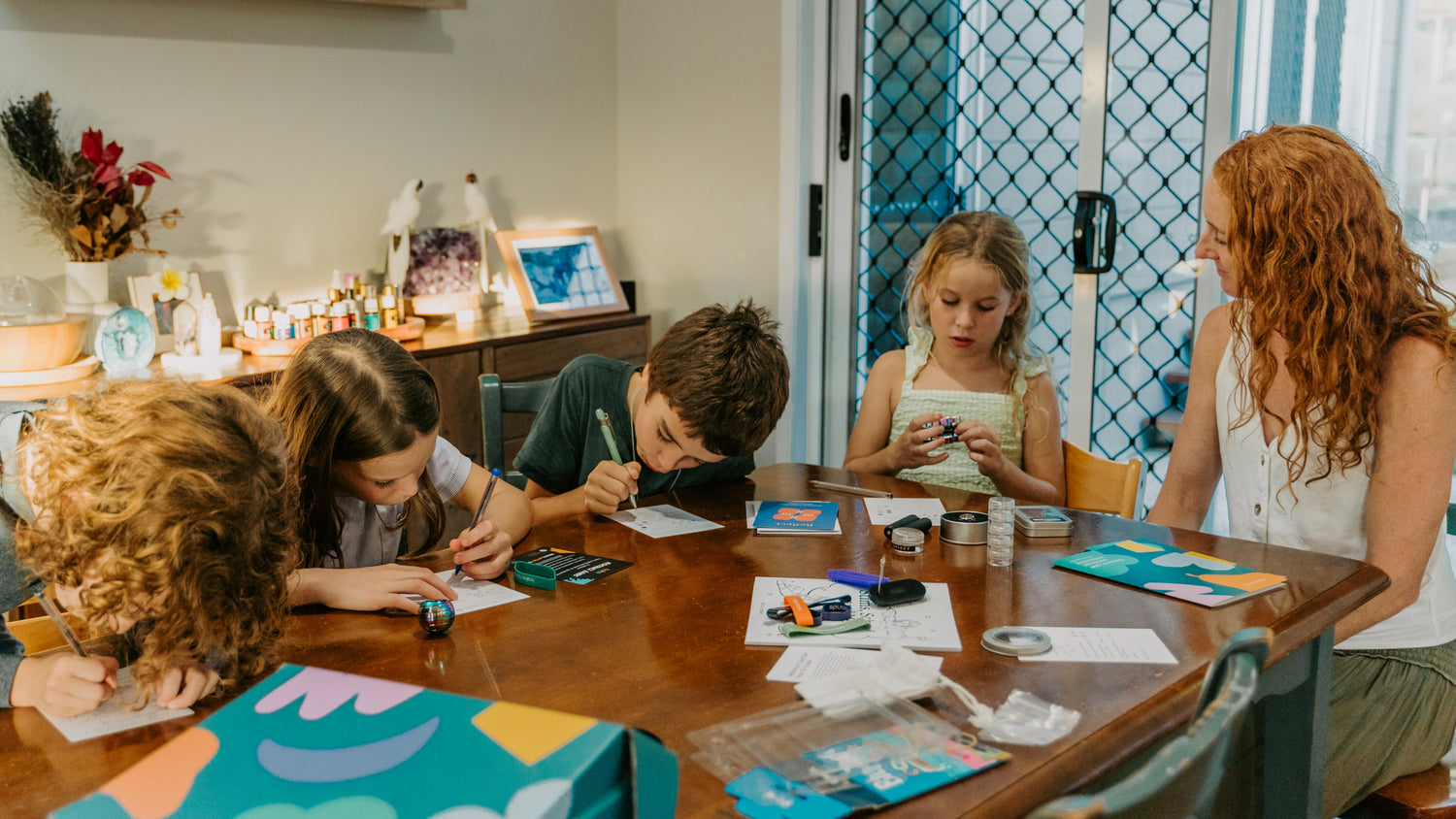 Children and a woman sitting around a table with art supplies in a home setting