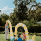 A person in a light blue shirt holds a blue ball in their left hand and an orange ball in their right. The scene, featuring green grass and fallen leaves, embodies the essence of The Play Way's Summer Holidays Program.