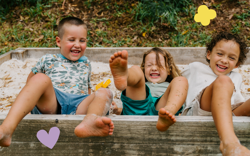 Three children sitting on a wooden ledge with cutout hearts and a flower above them.