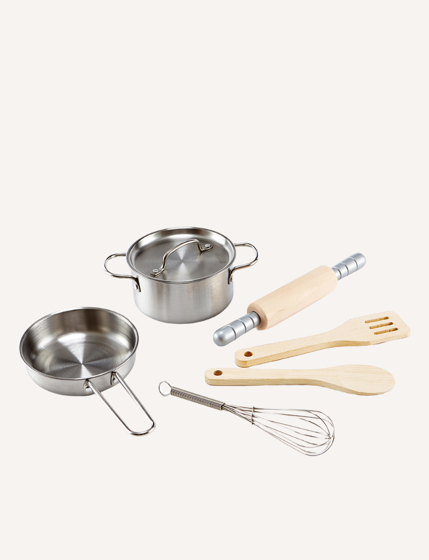 A Chef’s Cooking Set by Hape featuring a selection of miniature kitchen utensils and cookware, including a small saucepan, a pot with a lid, a rolling pin, a wire whisk, a wooden spatula, and a spoon, all neatly arranged on a plain surface.