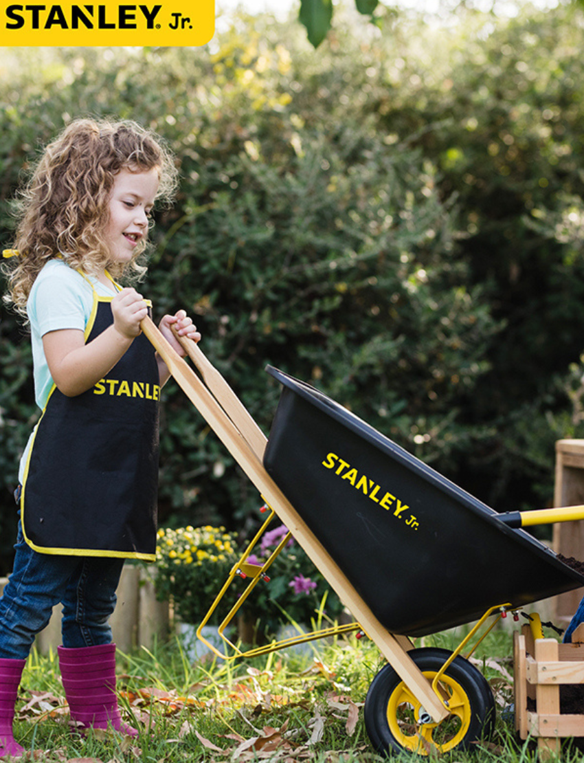 The Stanley Wheelbarrow, a kids' model by Stanley, showcases a sleek black design with vivid yellow accents, a single yellow wheel, and durable wooden handles against a white background.