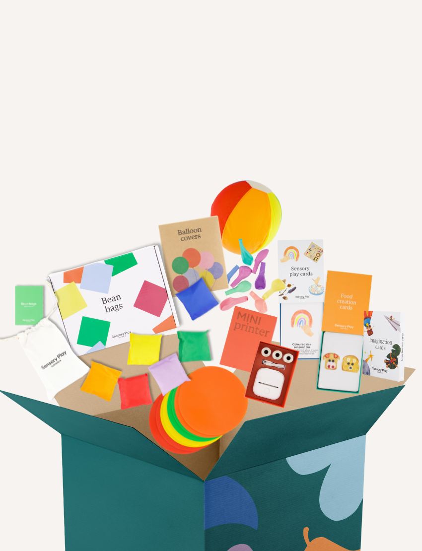 The Play Way’s September School Holidays Kit is an open green box with bean bags, a beach ball, flashcards, mini printer, balloons, sticky notes & a sensory kit—perfect for sensory play and hands-on fun. Some items are shown in their packaging.