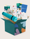 An open teal The Play Way box with the kit contents arranged above it: a rolled light teal yoga mat, the green Yoga and Mindfulness guide, the Exploring Feelings card and its word chart, a weighted eye mask in a linen pouch, the blue Yoga and Mindfulness Journal, the breathing card set showing star, rainbow and bubble cards, and the yoga card set showing a dog and a crab.