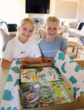 The Therapy At Home STEM: 3D Printing Pen Program includes a green pen, booklets, filaments, and kits to create running animals and walking robots—ideal for fine motor skills and STEM learning. The box is decorated with colorful abstract shapes.