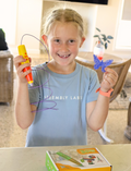 The Therapy At Home STEM: 3D Printing Pen Program includes a green pen, booklets, filaments, and kits to create running animals and walking robots—ideal for fine motor skills and STEM learning. The box is decorated with colorful abstract shapes.