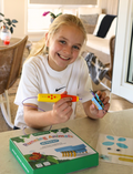 The Therapy At Home STEM: 3D Printing Pen Program includes a green pen, booklets, filaments, and kits to create running animals and walking robots—ideal for fine motor skills and STEM learning. The box is decorated with colorful abstract shapes.