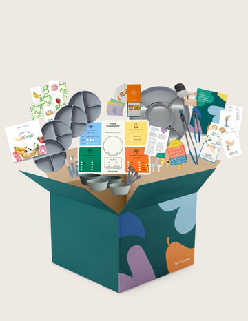 The Therapy At Home "Feeding and mealtimes: Helping you get started Program" includes a large teal and green box packed with educational materials, activity cards, utensils, pans, bowls, silicone trays—ideal for supporting feeding difficulties.