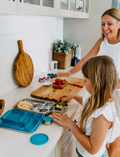 The Lunch Box Program by Therapy At Home comes in a teal and blue patterned box with stainless steel containers, a blue cup, activity cards, planners, a game, and labels—all neatly packed and partially displayed.