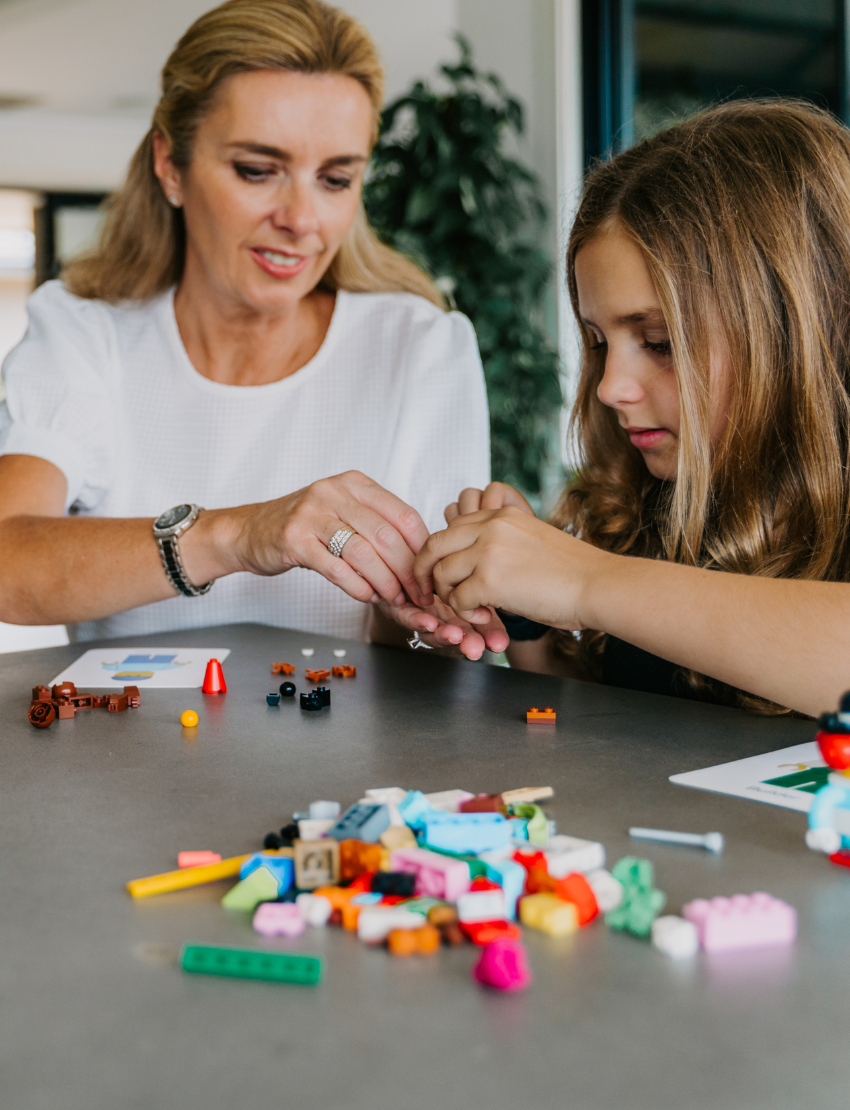 An open blue and green box from Therapy At Home's Build it with Bricks Foundation Program includes two LEGO Classic sets and colorful activity cards—ideal for supporting executive function skills in therapy sessions—displayed on a plain light background.